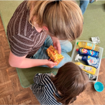 A teacher and a child are looking at warning symbols on packaging such as cleaning products.