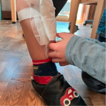 A child is putting on a bandage on another child's leg.